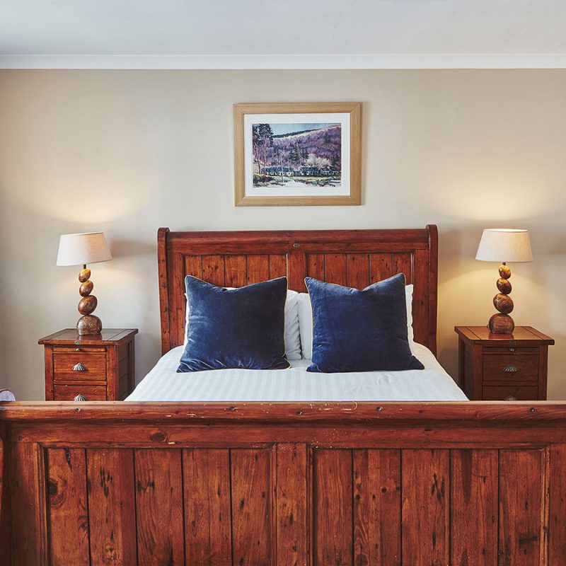 A stunning double wooden bed with wooden side table and lamps in a Deluxe Room in Brambles of Inveraray Hotel in Scotland