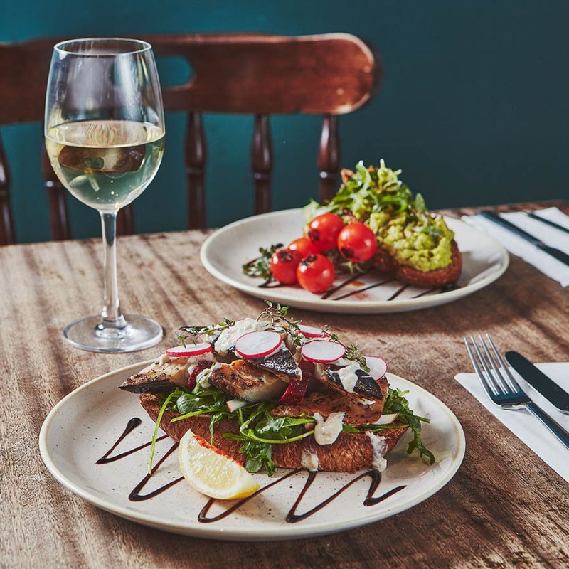 Two delicious plates of food with a glass of white wine on a table set for dining in Brambles of Inveraray Hotel restaurant.