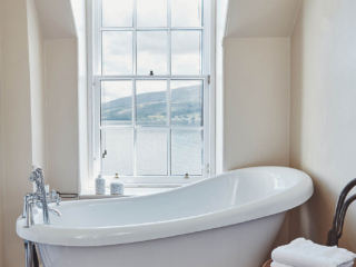 A stunning bathroom with roll top bath by a sash window overlooking glorious views of Loch Fyne at Lochview Apartment part of Brambles hotel in Inveraray in Scotland