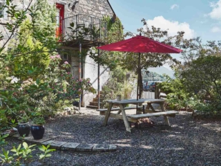 A beautiful lush courtyard with a picnic table with a red umbrella and a balcony off the apartment overlooking the courtyard at Lochview Apartment part of Brambles hotel in Inveraray in Scotland