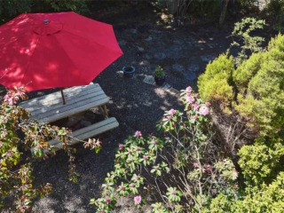 A view from the balcony of the lush courtyard and picnic table with a red umbrella at Lochview Apartment part of Brambles hotel in Inveraray in Scotland