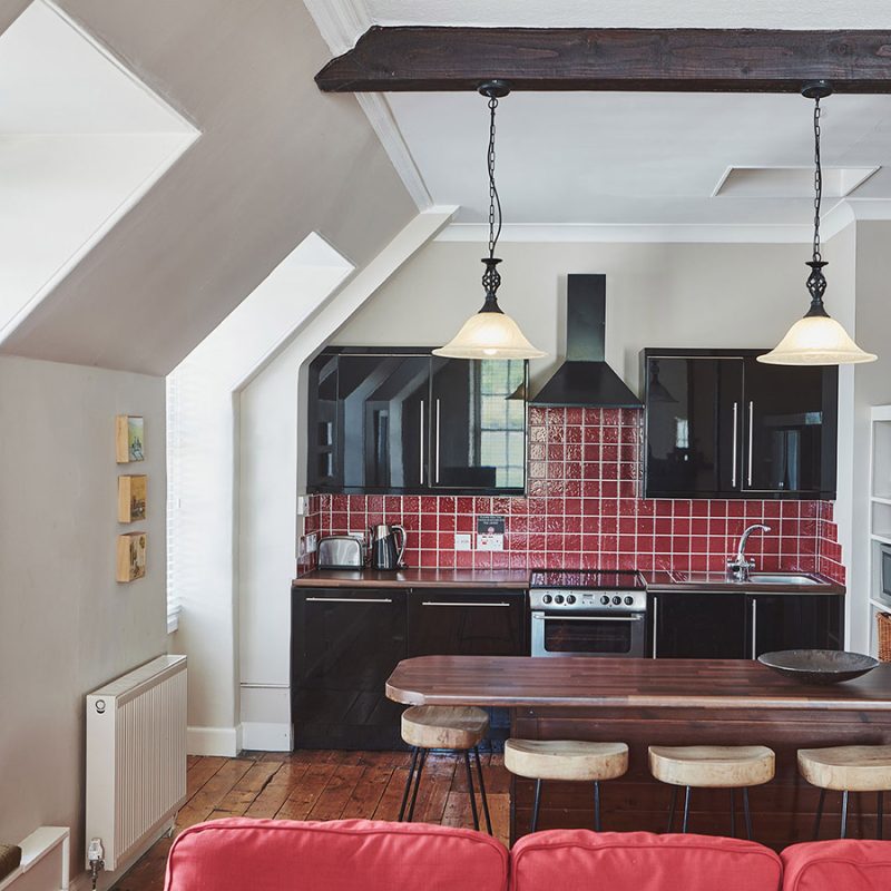 The kitchen in the open plan living area with an old wooden ceiling beam and antique lights hanging from it at Lochview Apartment part of Brambles of Inveraray Hotel in Scotland
