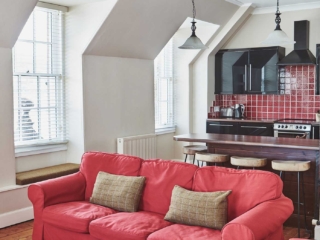 The kitchen in the open plan living area with an old wooden ceiling beam and antique lights hanging from it at Lochview Apartment part of Brambles hotel in Inveraray in Scotland