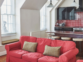 The kitchen in the open plan living area with an old wooden ceiling beam and antique lights hanging from it at Lochview Apartment part of Brambles hotel in Inveraray in Scotland