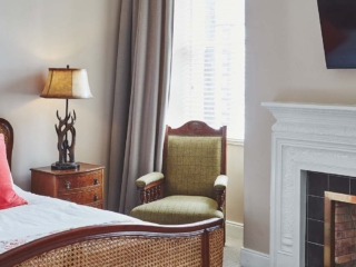 An antique rattan double bed, an antique armchair by a fireplace and an antler bedside light in a Superior Room in Brambles hotel in Inveraray in Scotland