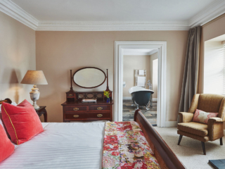 A stunning double bedroom with antique furniture leading into a bathroom with a roll top bath in a Superior Room in Brambles hotel in Inveraray in Scotland